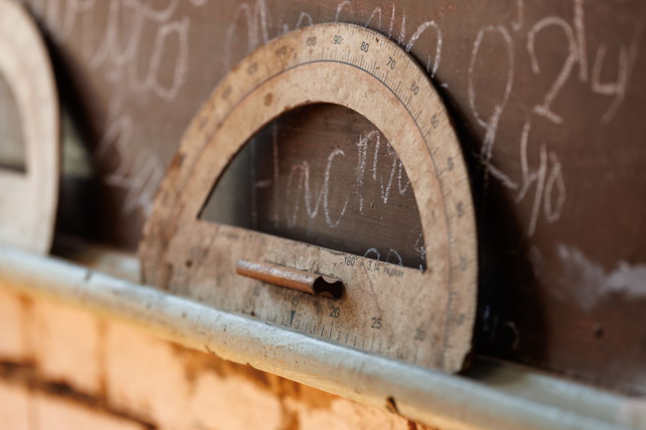 A vintage protractor resting against a chalkboard filled with chalk writing.