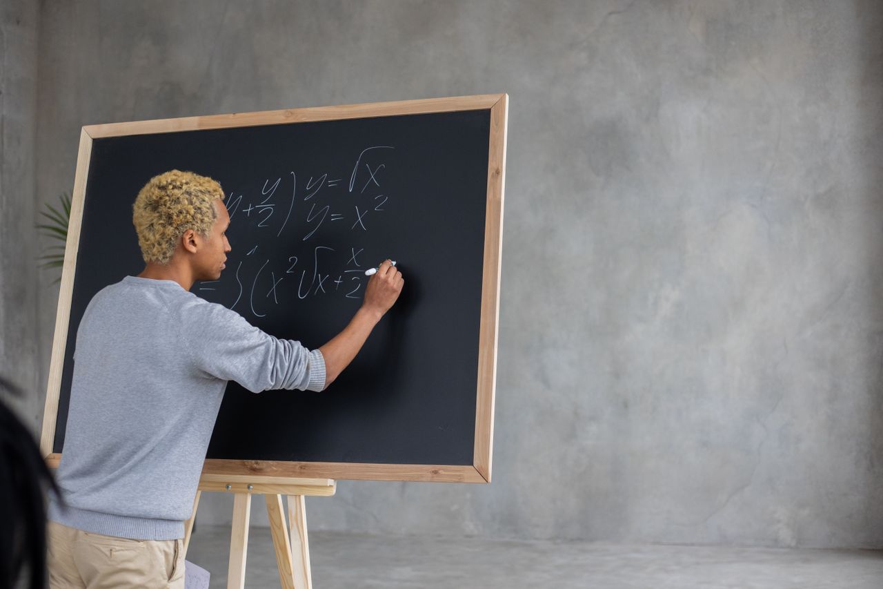 Back view of African American student with marker writing task on blackboard while studying in classroom